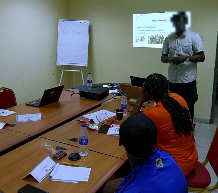 An Apabet facilitator briefing trainees with a projected slide and flipchart